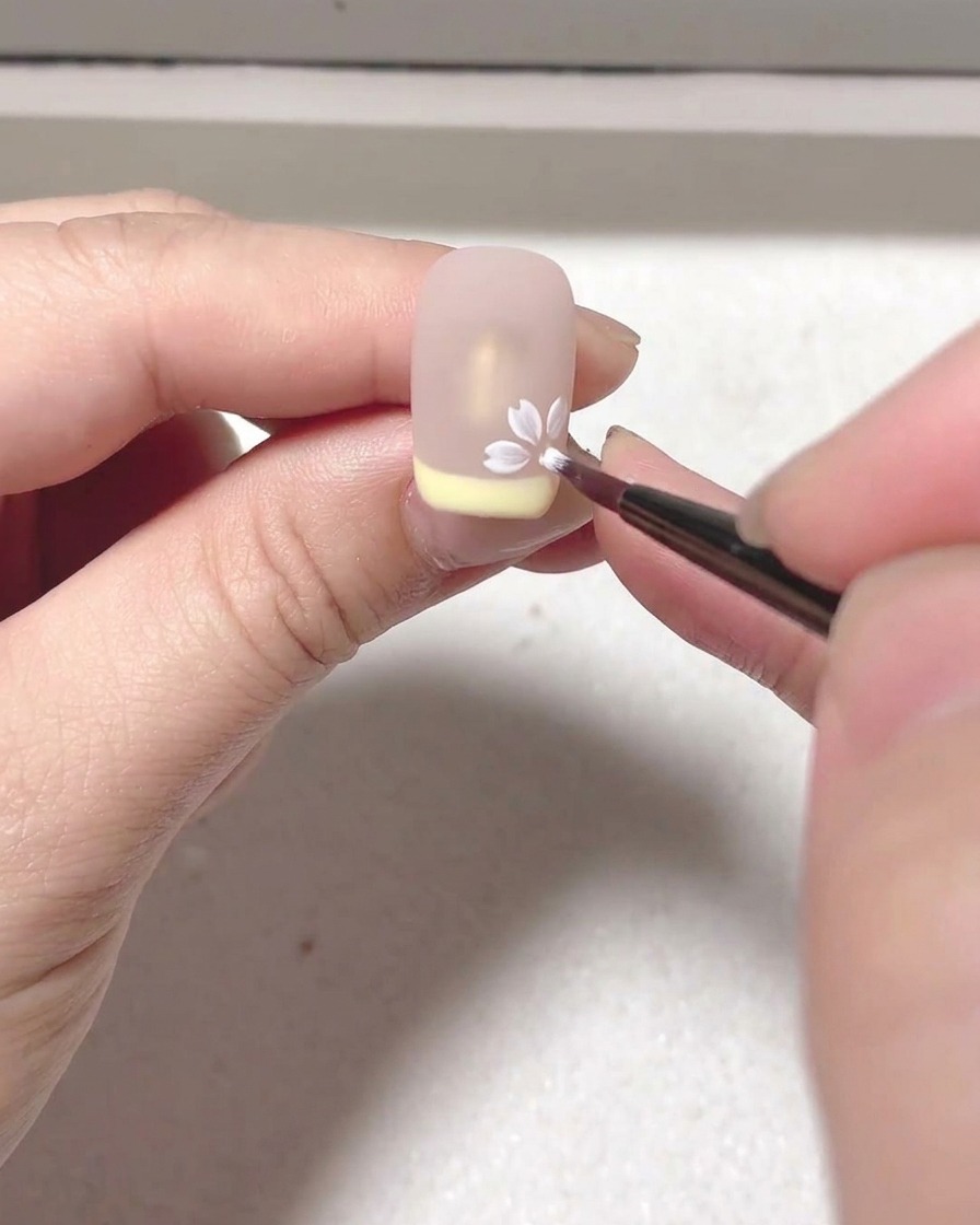 Primo piano di un pennello che applica blooming gel bianco per creare petali su una superficie nude.