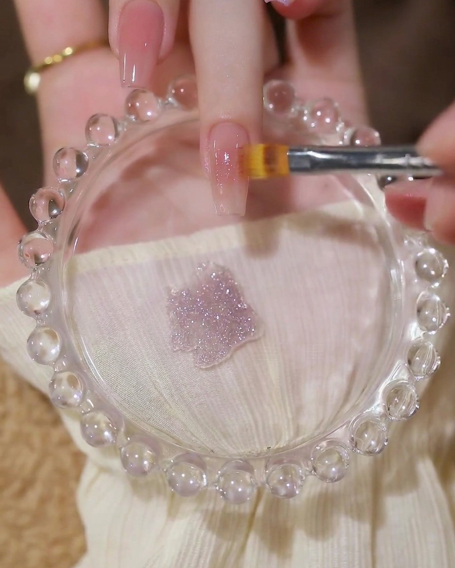 Un pennello che applica uno strato di gel trasparente e glitterato su una base nude.