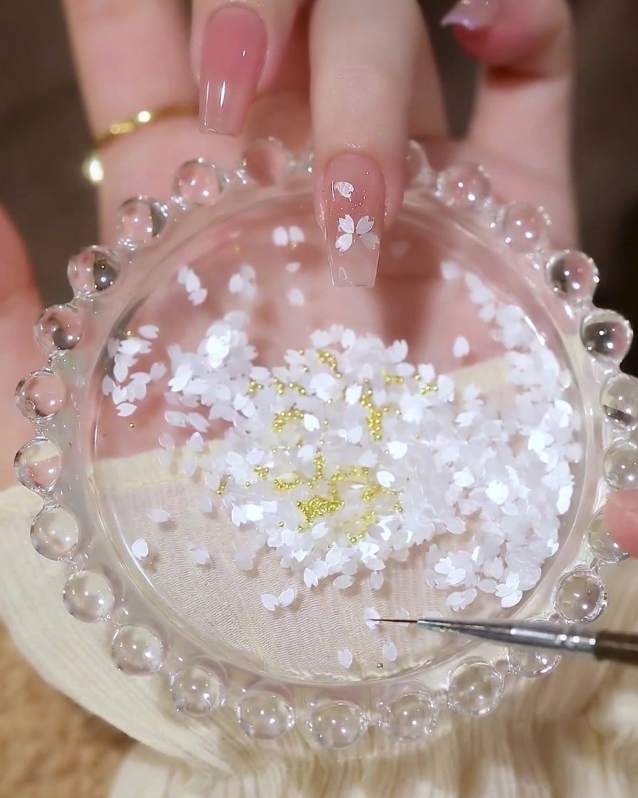 Ununghia con un design floreale completato, realizzato con paillettes a petalo e una piccola perlina dorata al centro.