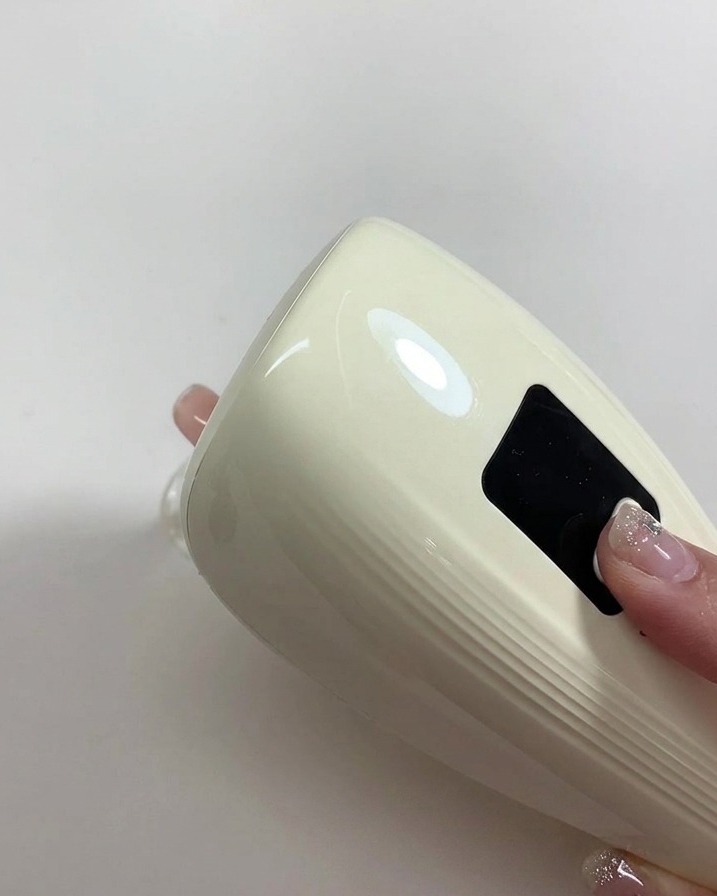 Una mano tiene una piccola lampada UV/LED portatile direttamente sopra ununghia appena dipinta di gel nude per far asciugare lo smalto.