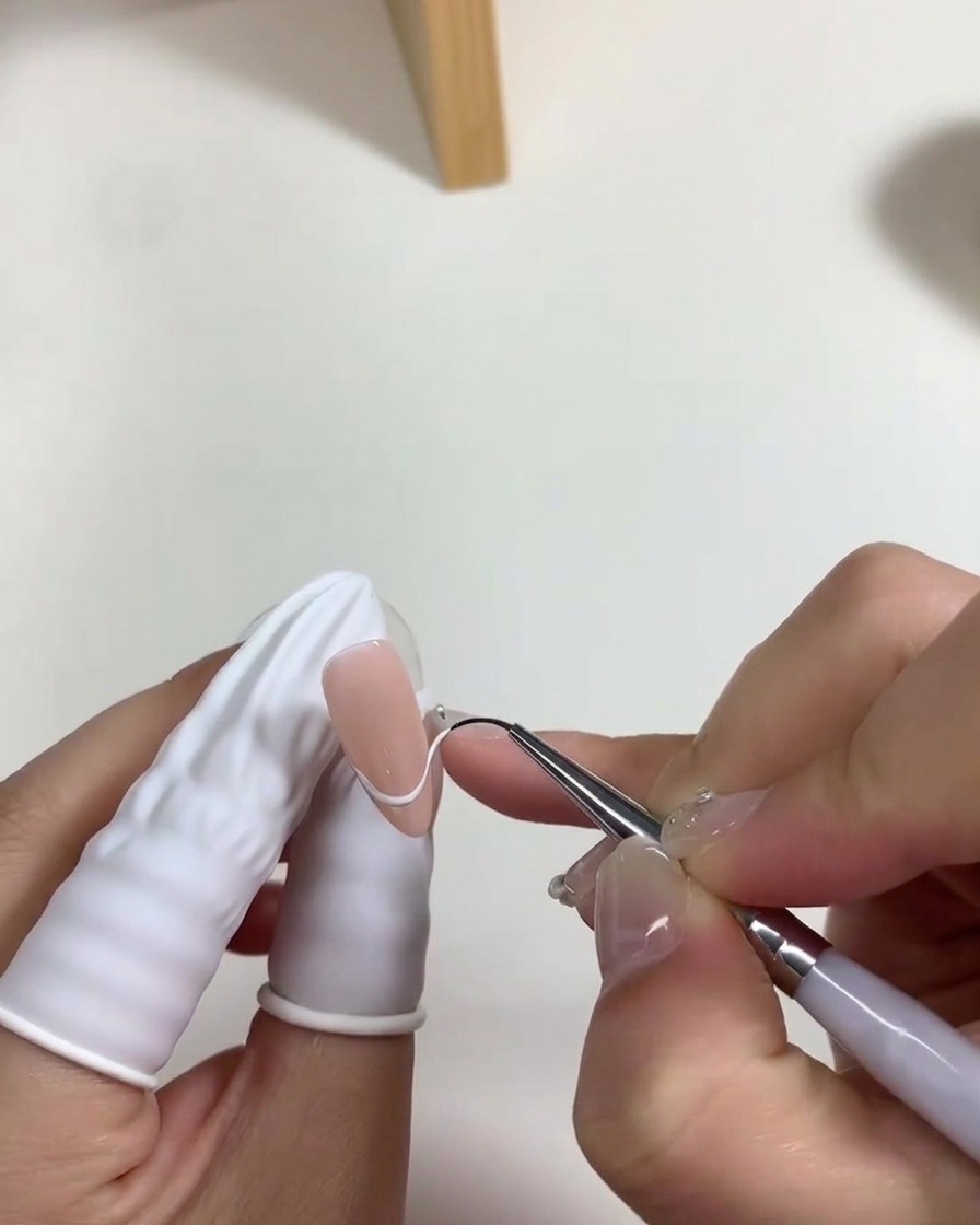 Un pennello applica un sottile strato di smalto gel bianco lattiginoso sul letto ungueale.