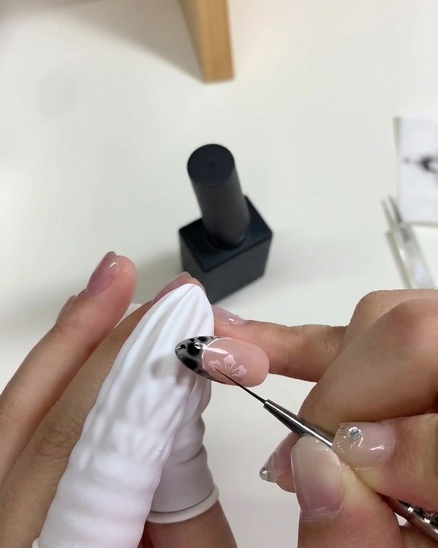 Una mano posiziona ununghia sotto una mini lampada UV/LED portatile per polimerizzare la nail art con i fiori di ciliegio rosa.