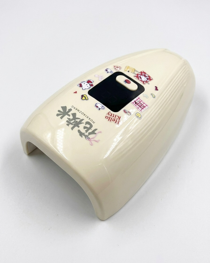 Una mini lampada UV/LED per unghie color crema decorata con adesivi di Hello Kitty su una superficie bianca e luminosa.