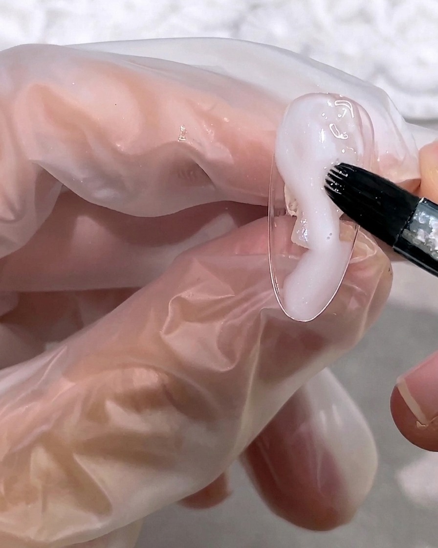 Un pennello applica una piccola quantità di gel bianco lattiginoso semitrasparente sulla punta di ununghia.