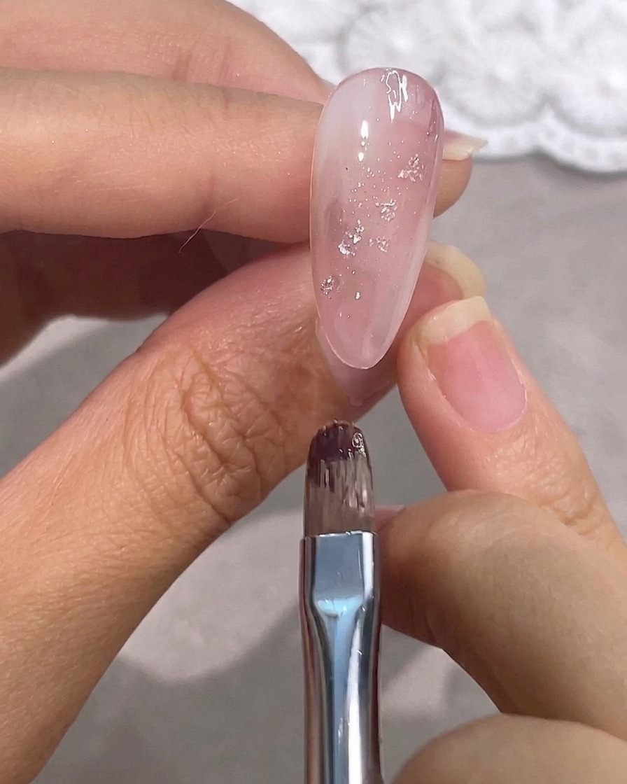 Un pennellino per dettagli passa sopra ununghia in gel rosa lucido con accenti in foglia argento.