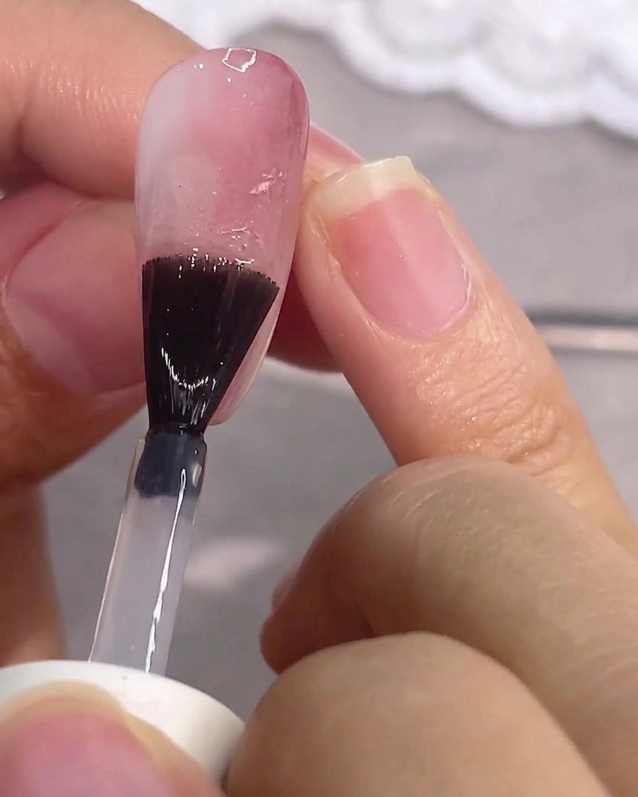 Un pennello stende un top coat opaco trasparente su ununghia in gel rosa.