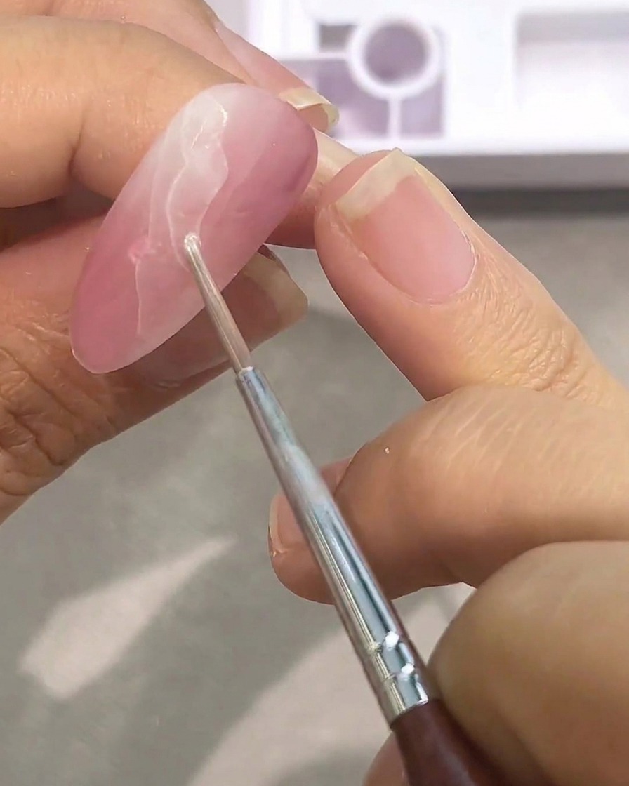 Primo piano di un pennello che applica un secondo strato di acquerello bianco su una base rosata, per costruire il motivo marmorizzato.