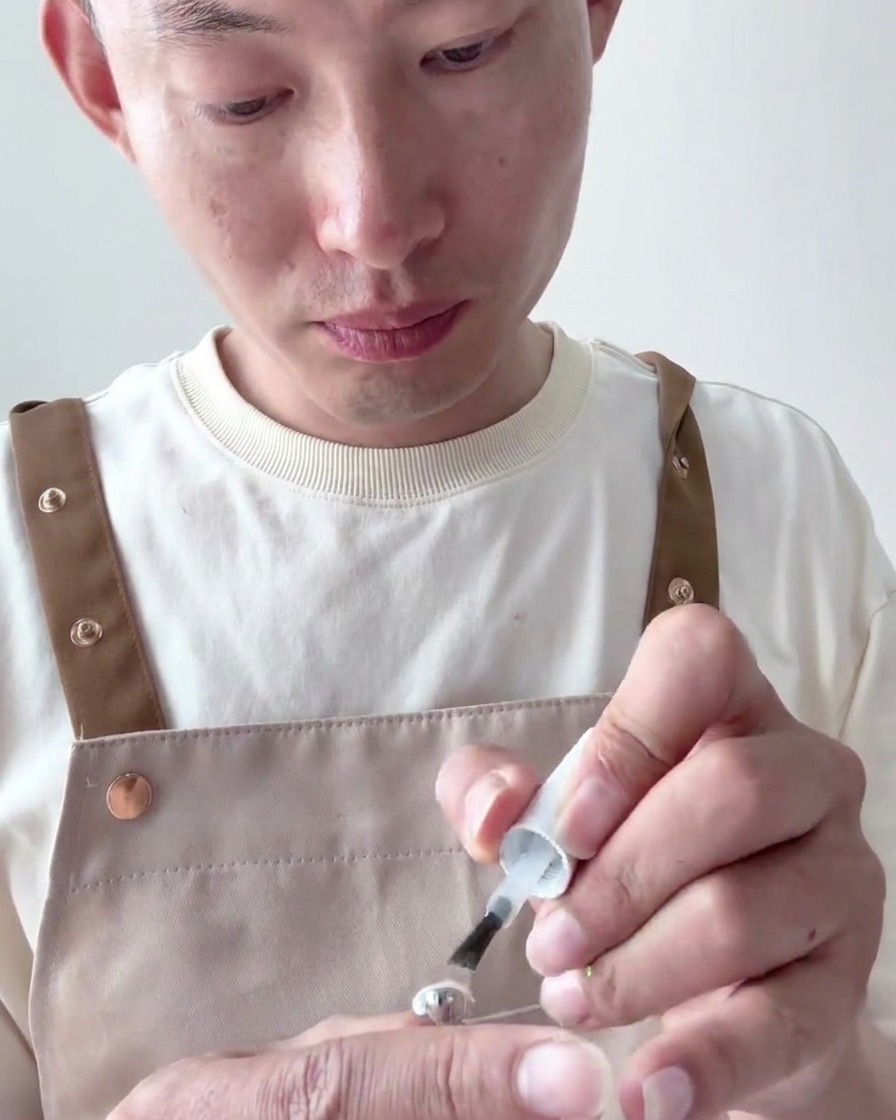 Primo piano di un pennello che applica un secondo strato di smalto gel bianco latte coprente sulla tip.