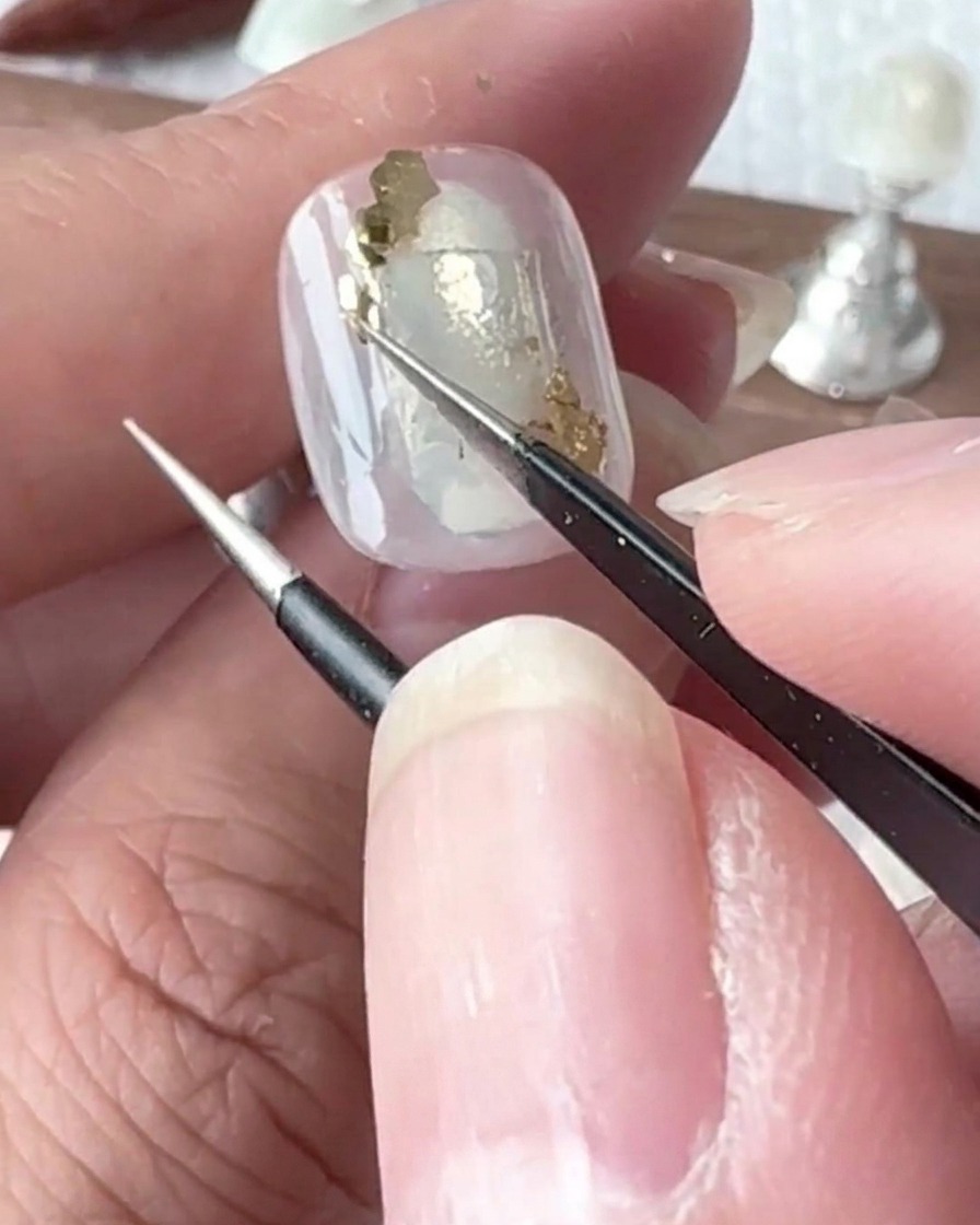 Un piccolo pennello di precisione applica minuscole gocce di gel trasparente sulla superficie di ununghia colorata.