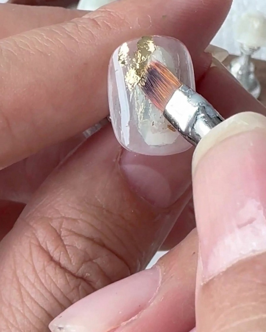 Primo piano di uno strumento in silicone che preme su scaglie di foglia oro applicate su ununghia.