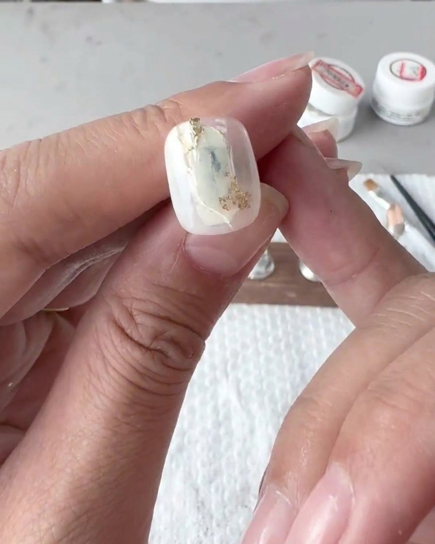 Primo piano di un pennello piatto che sfuma delicatamente le linee di smalto gel bianco su una tip.