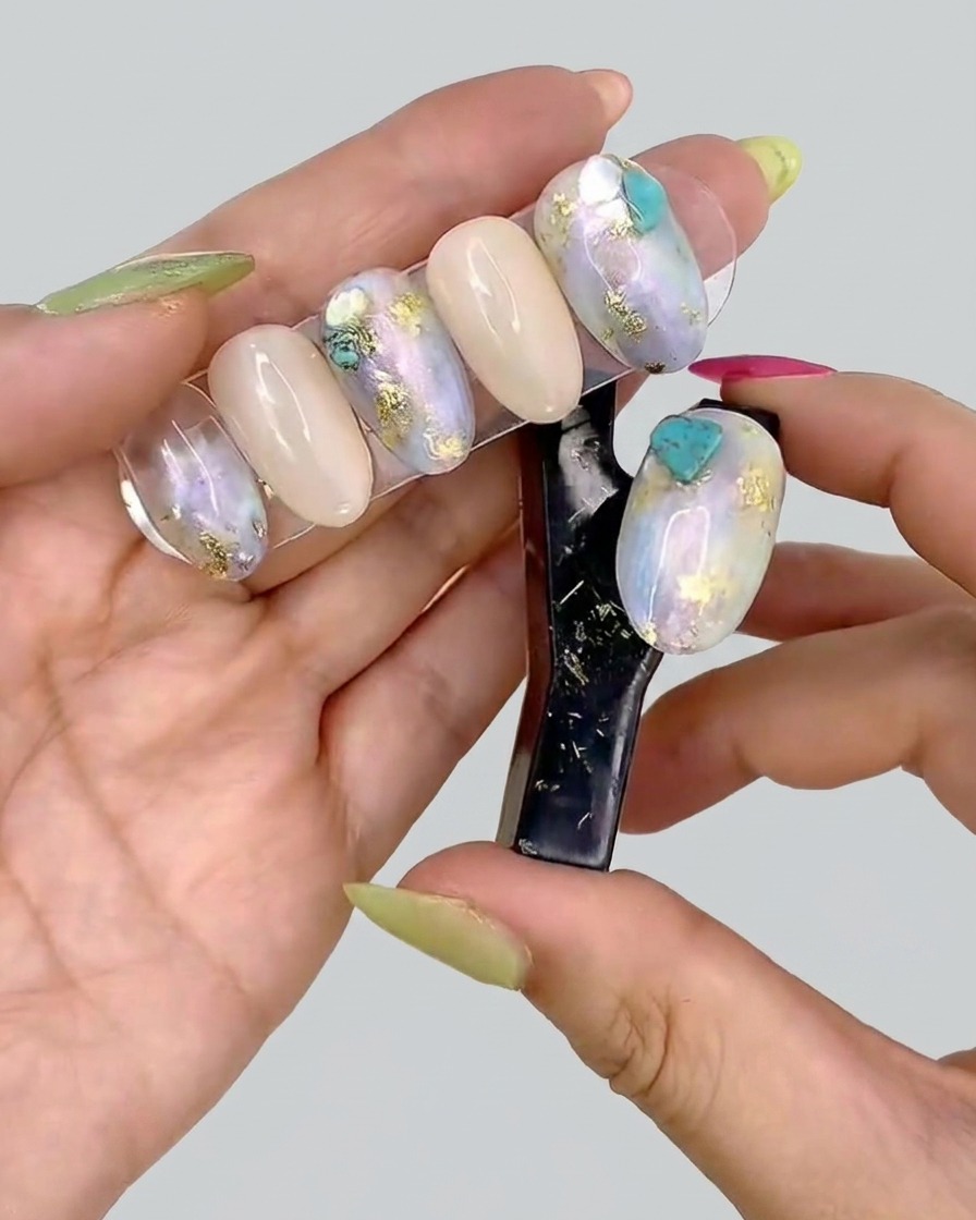 Una pinzetta posiziona piccoli pezzi di foglia oro su ununghia decorata con gel.