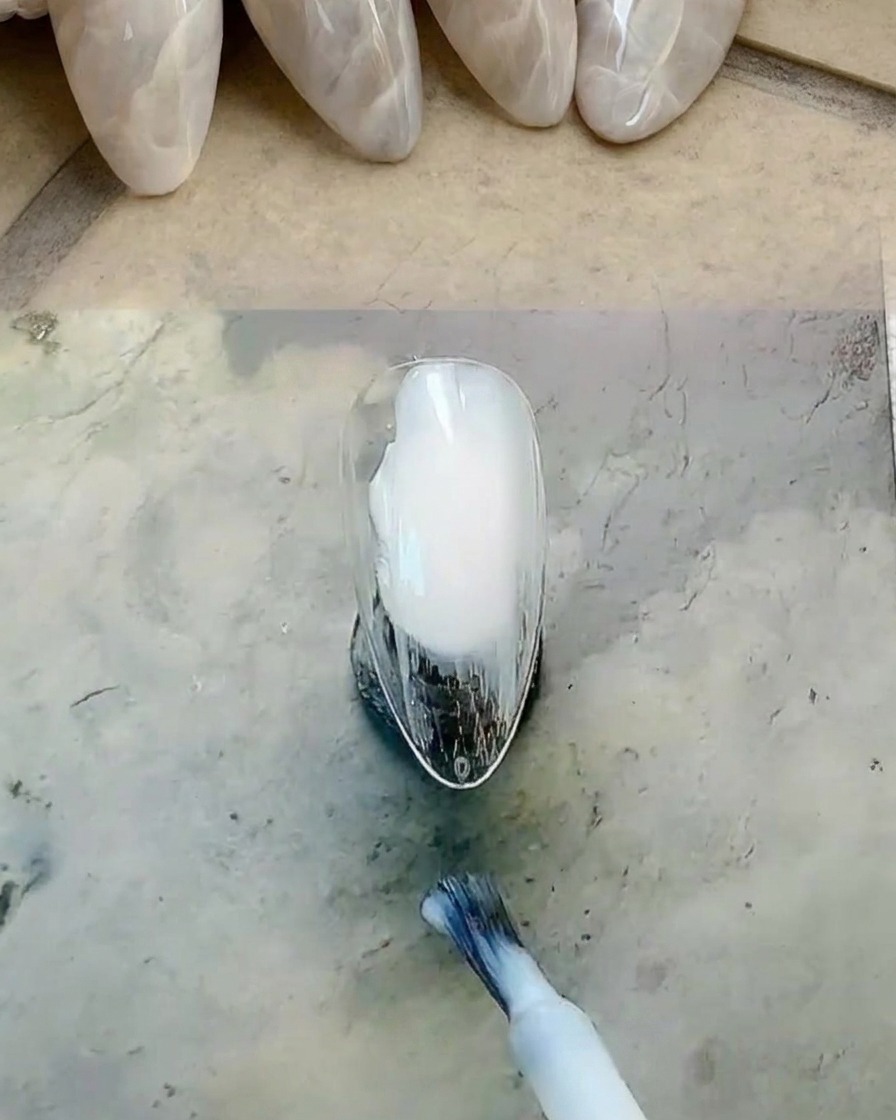 Pennello che applica uno smalto gel bianco lattiginoso sulla superficie dellunghia.