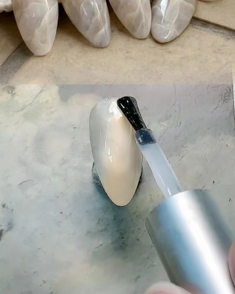 Un pennello che applica uno strato di gel trasparente sullunghia per prepararla alla sfumatura.