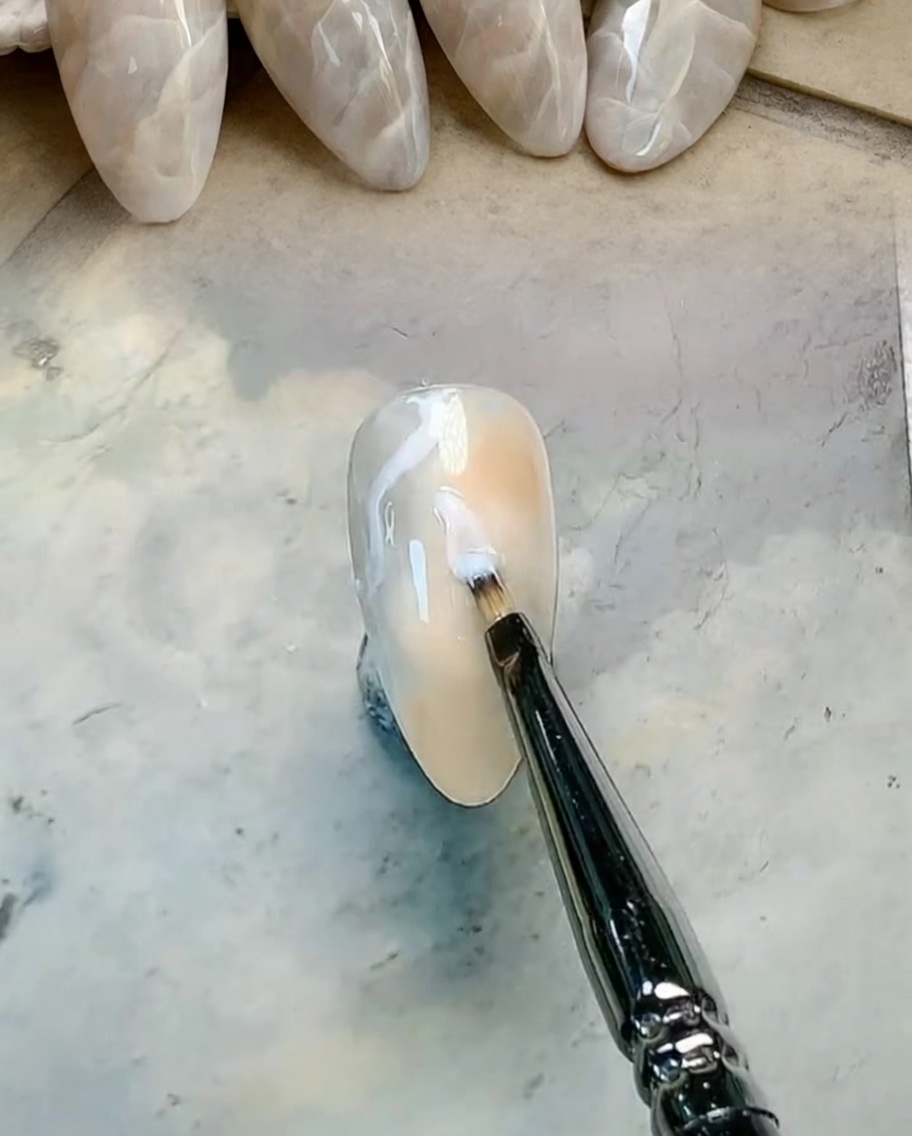 Un pennello piatto che sfuma i colori gel marrone e grigio per creare un gradiente morbido.