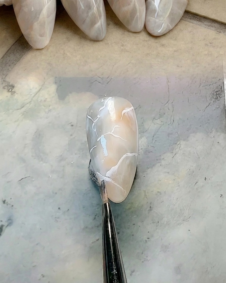 Un piccolo pennello tondo pulito che sfuma il bordo di una linea di gel bianco.