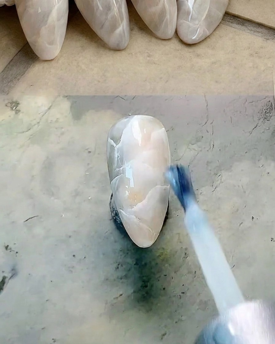 Un pennello piatto che applica uno strato sottile di gel bianco lattiginoso traslucido.
