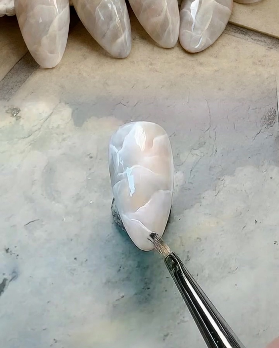 Un pennello liner fine che disegna venature bianche nitide sopra una base marmorizzata.