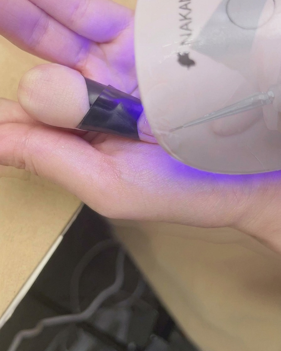 Un dito posizionato sotto una mini lampada UV/LED per polimerizzare la nail art con gradiente blush.