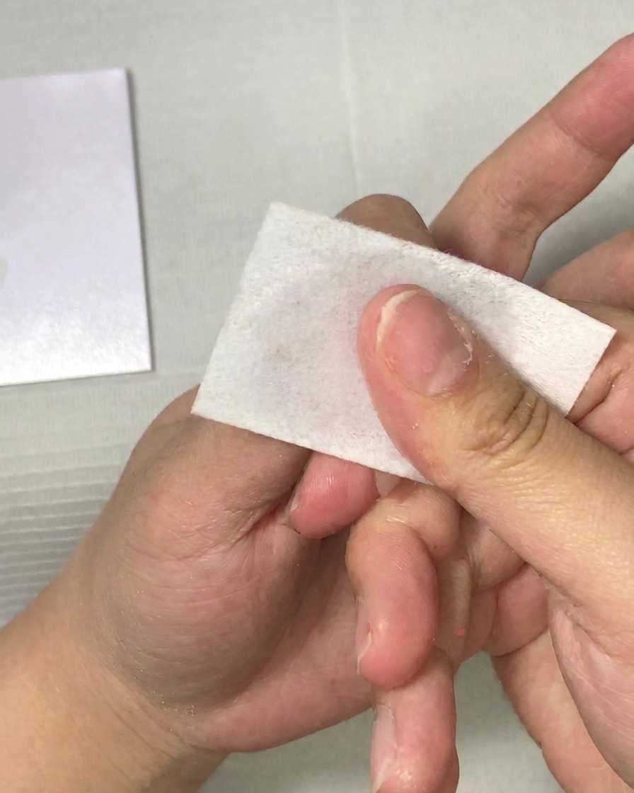 Primo piano di una mano che utilizza un pad senza lanugine per pulire ununghia.
