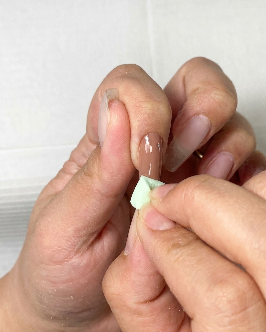 Un pennello che applica uno strato sottile di gel color marrone su ununghia naturale.