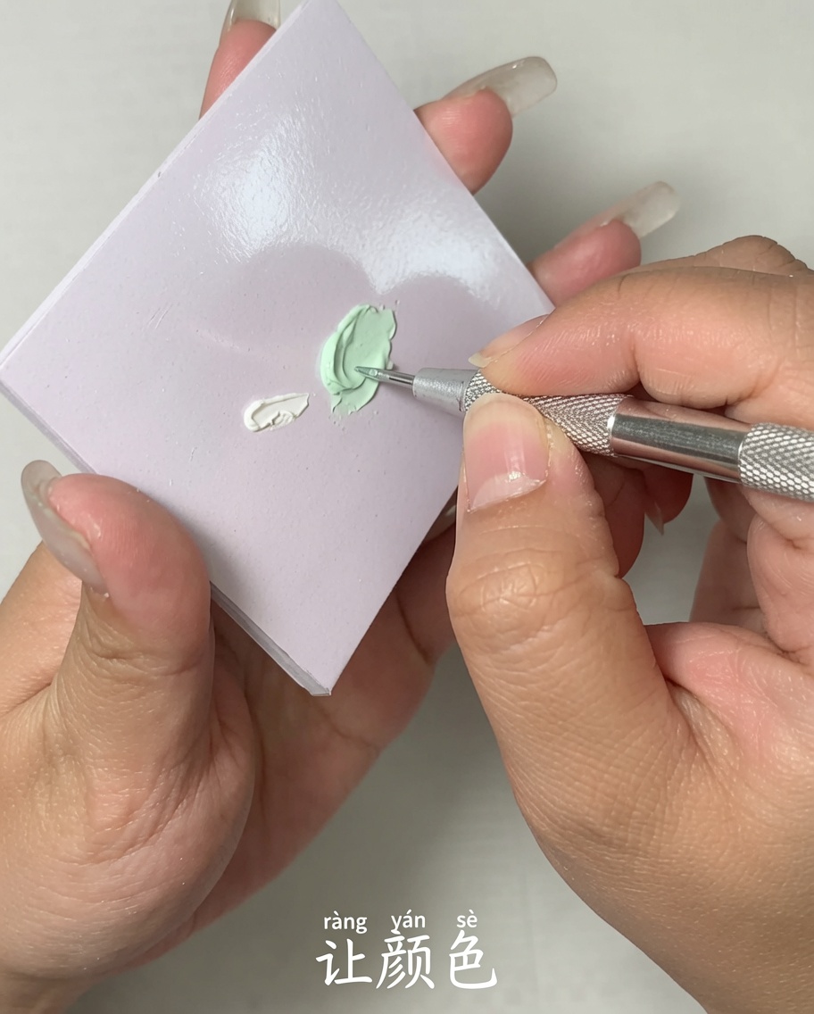 Primo piano di uno strumento in metallo che miscela due diversi colori di gel su una tavolozza piatta.