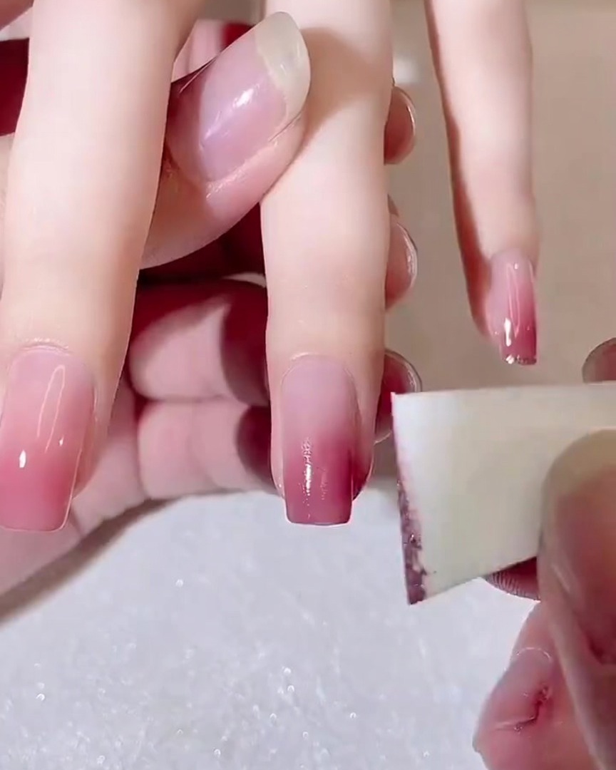 Primo piano di una spugnetta da trucco usata per tamponare un secondo strato di gel rosa scuro sulla punta di ununghia.