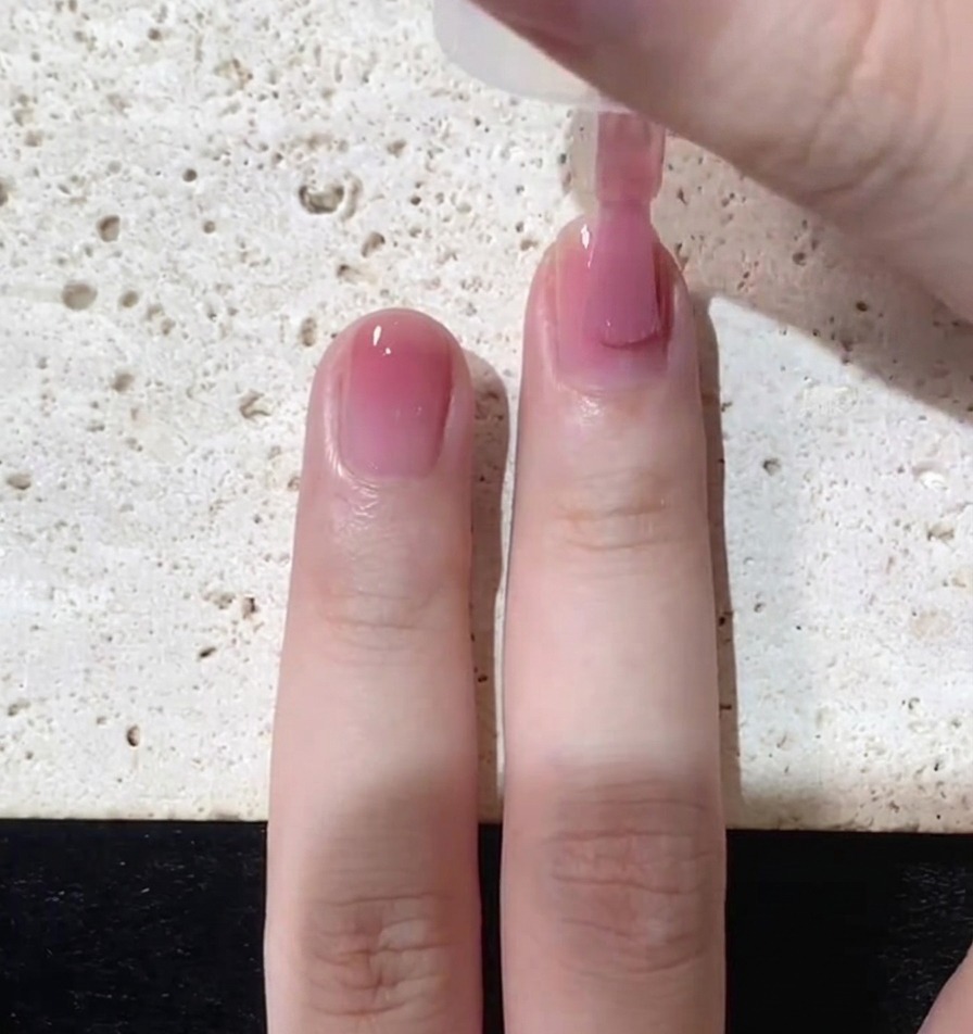 Primo piano di un pennello che applica uno strato sottile di smalto rosa traslucido su ununghia naturale