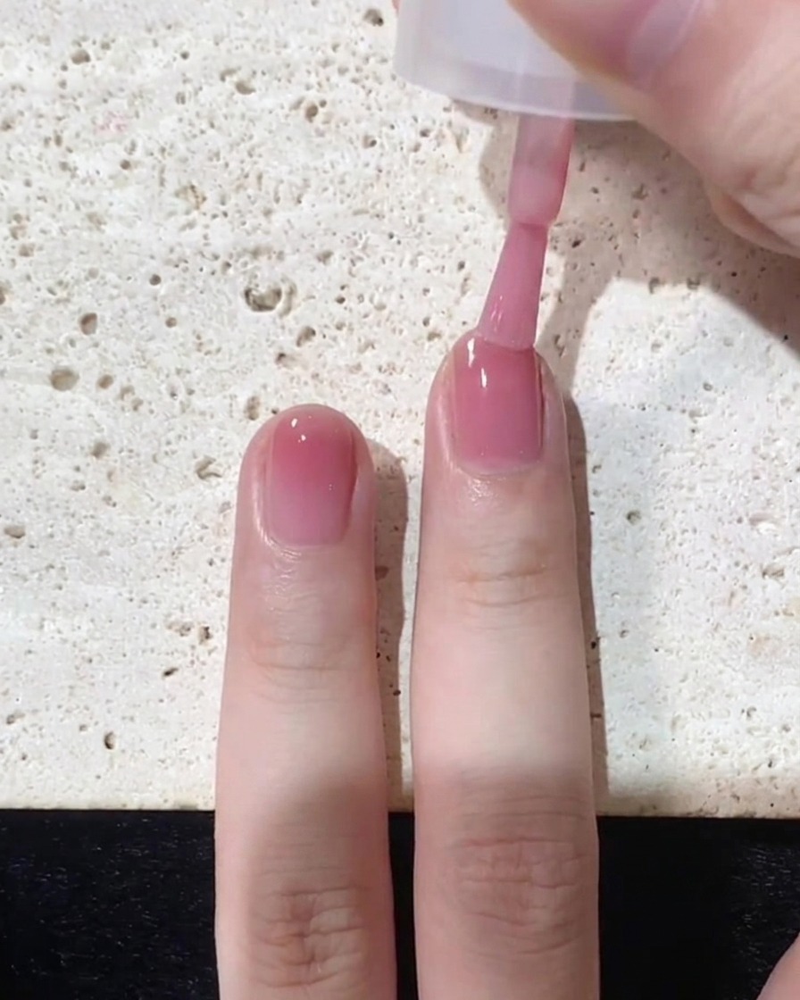 Un pennello che applica uno strato finale concentrato di smalto rosa specificamente sulla punta dellunghia
