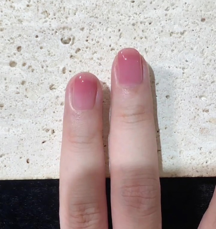 Vista ravvicinata dellapplicazione del top coat finale che viene uniformato su ununghia sfumata rosa