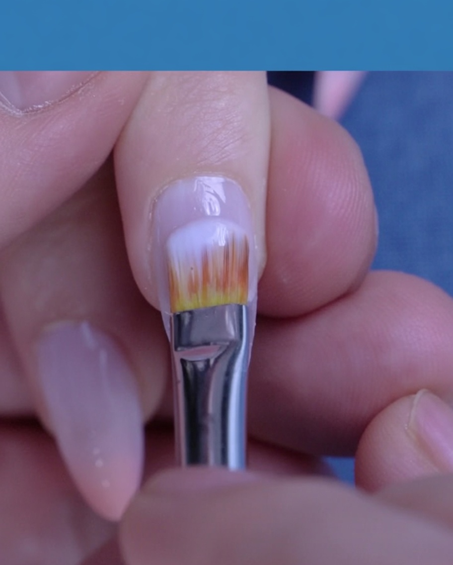 Un pennello applica un gel color bianco latte traslucido sullunghia naturale.