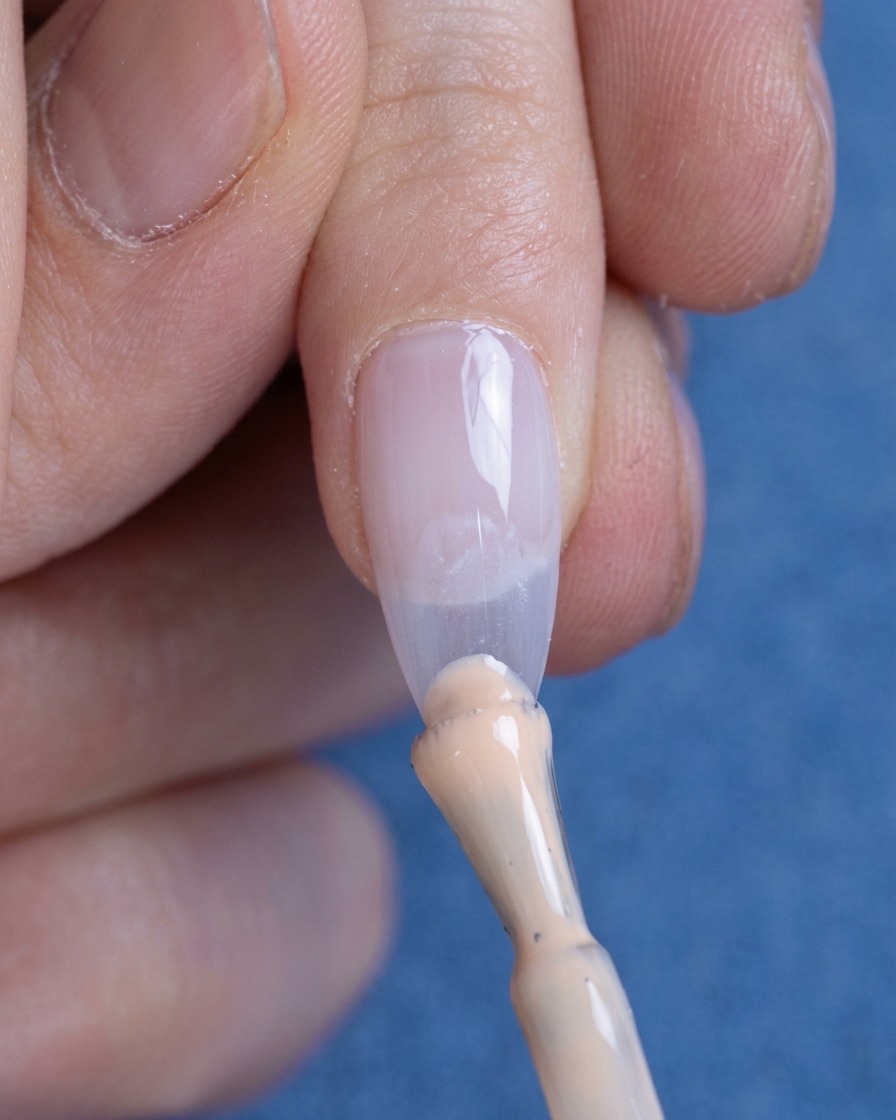 Una piccola goccia di smalto gel nude applicata sulla punta dellunghia.