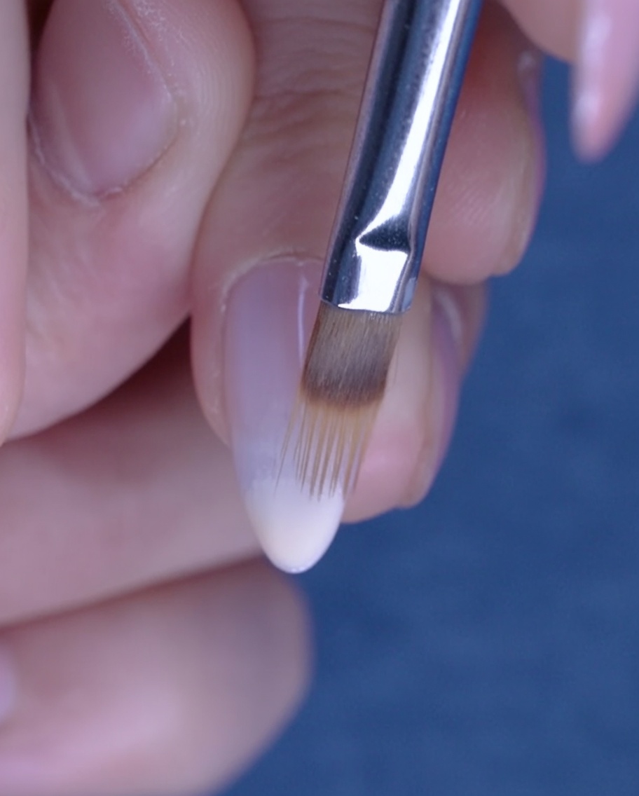 Un pennello piatto sfuma il gel nude verso lalto sullunghia per creare un effetto ombré.