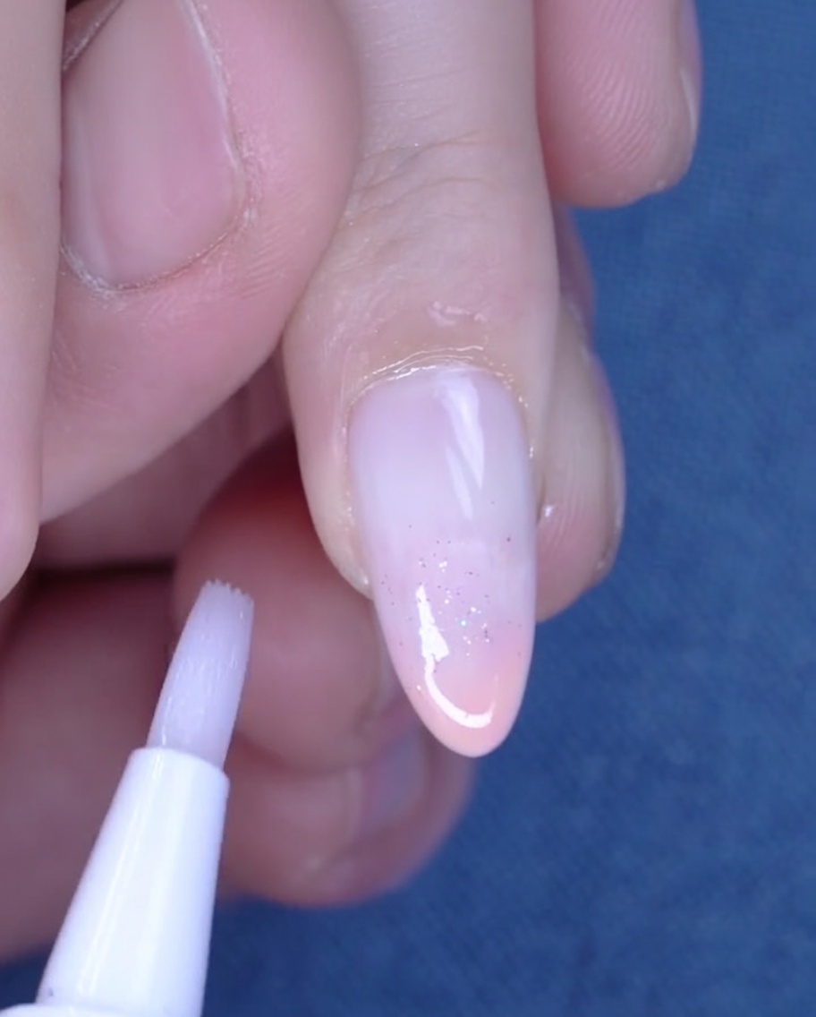 Una penna per cuticole che applica olio sulla pelle idratata attorno a ununghia appena fatta.