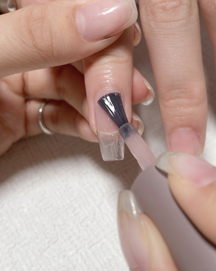 Pennello che applica base coat trasparente su ununghia naturale pulita.