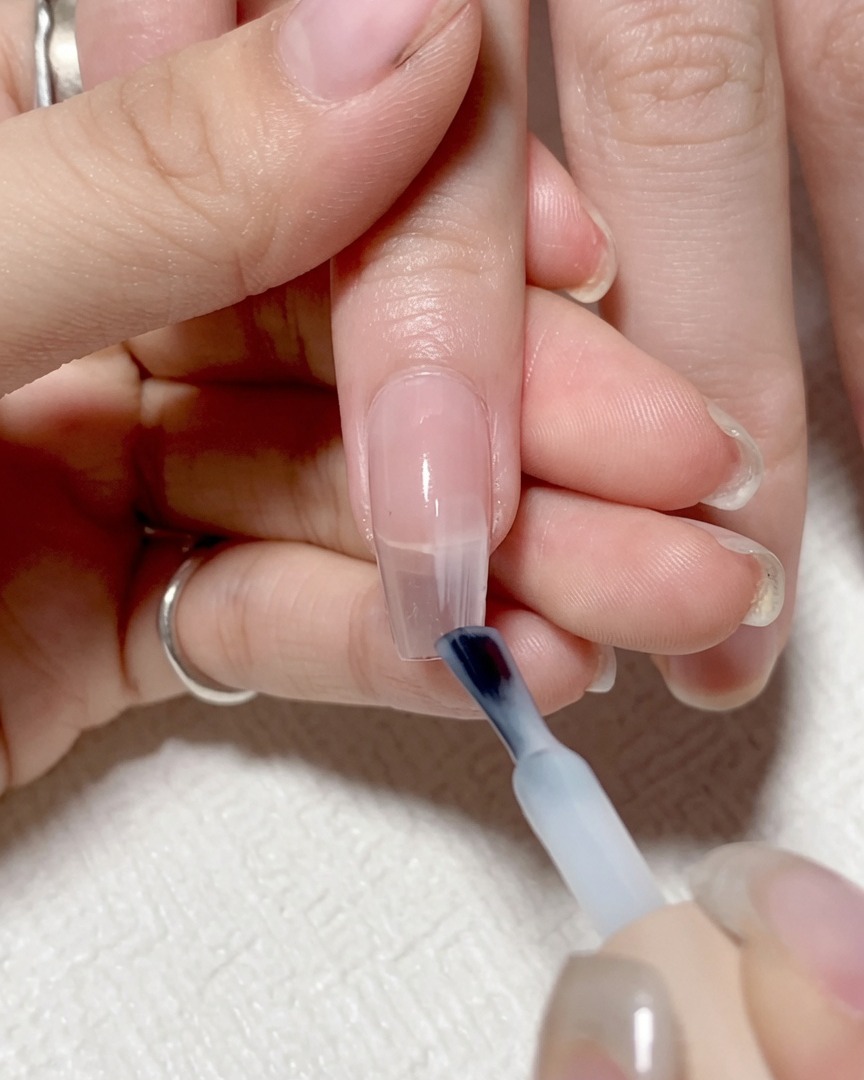 Pennello da unghie che applica gel trasparente chiaro sulla metà destra dellunghia.