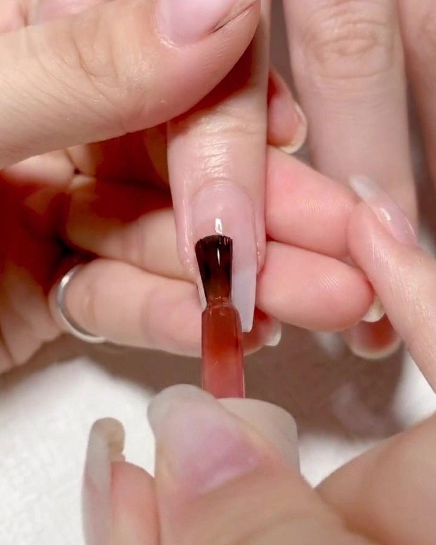 Pennello che applica gel rosso vivace sulla metà sinistra dellunghia.