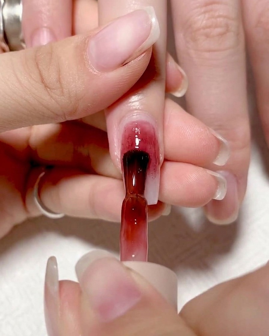 Pennello che applica gel rosso su metà unghia, creando un blocco di colore definito.