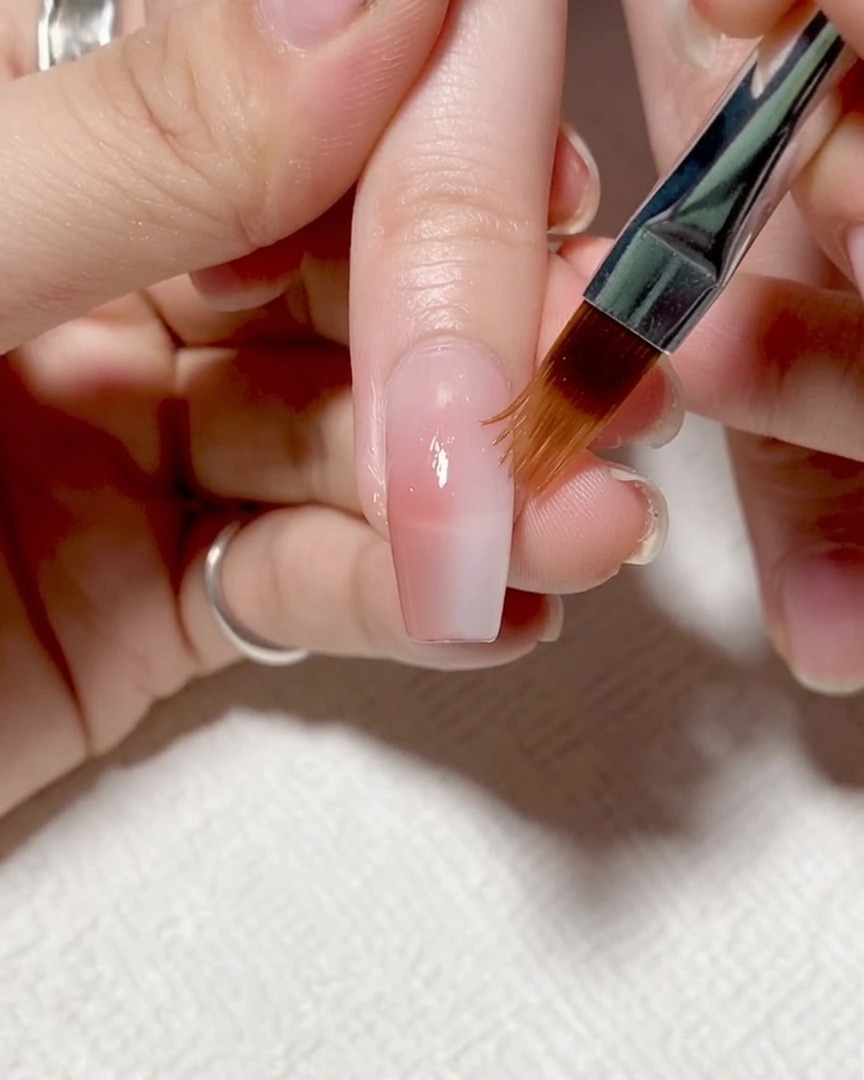 Pennello che applica un gel rinforzante trasparente e leggermente denso su tutta lunghia.