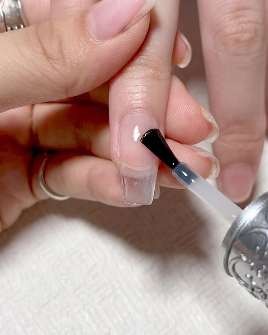 Primo piano di un pennello che applica un top coat trasparente e lucido su ununghia con sfumatura finita.