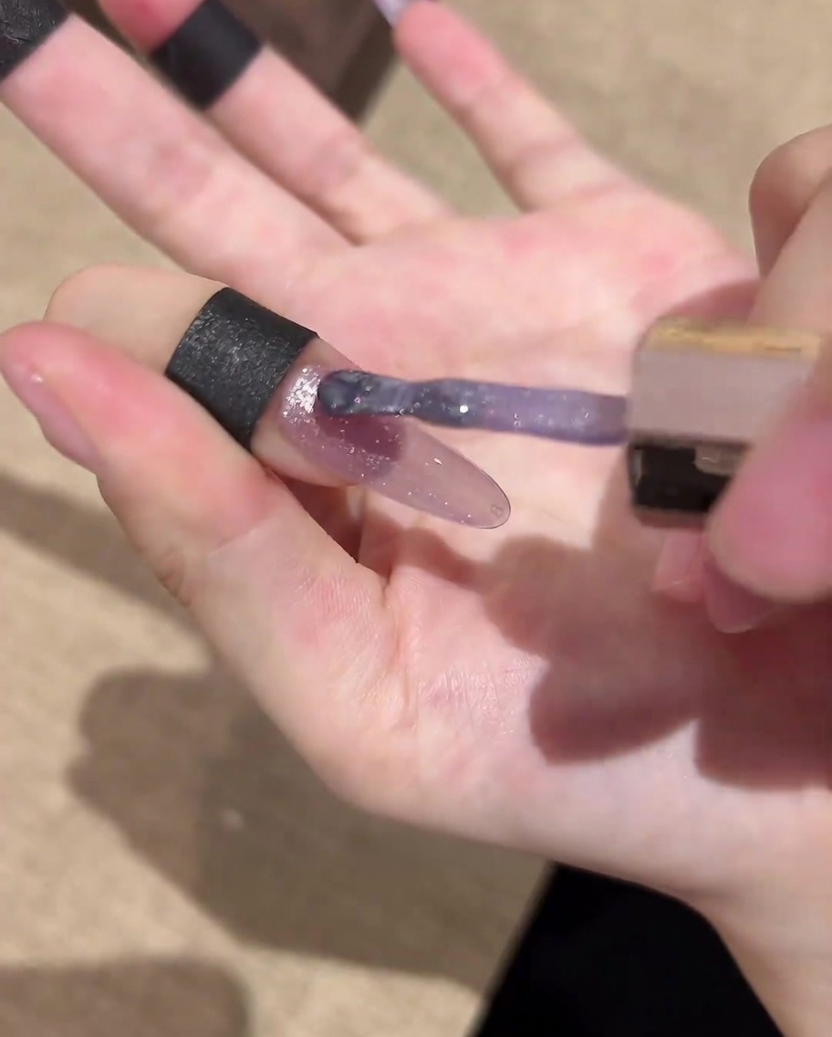 Un pennello che applica un top coat finale lucido sopra la nail art cat eye galattica completata.
