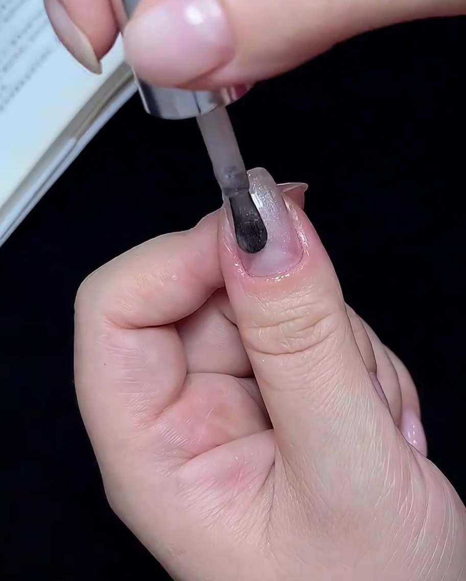 Un pennello che applica smalto cat-eye bianco traslucido su una singola unghia.