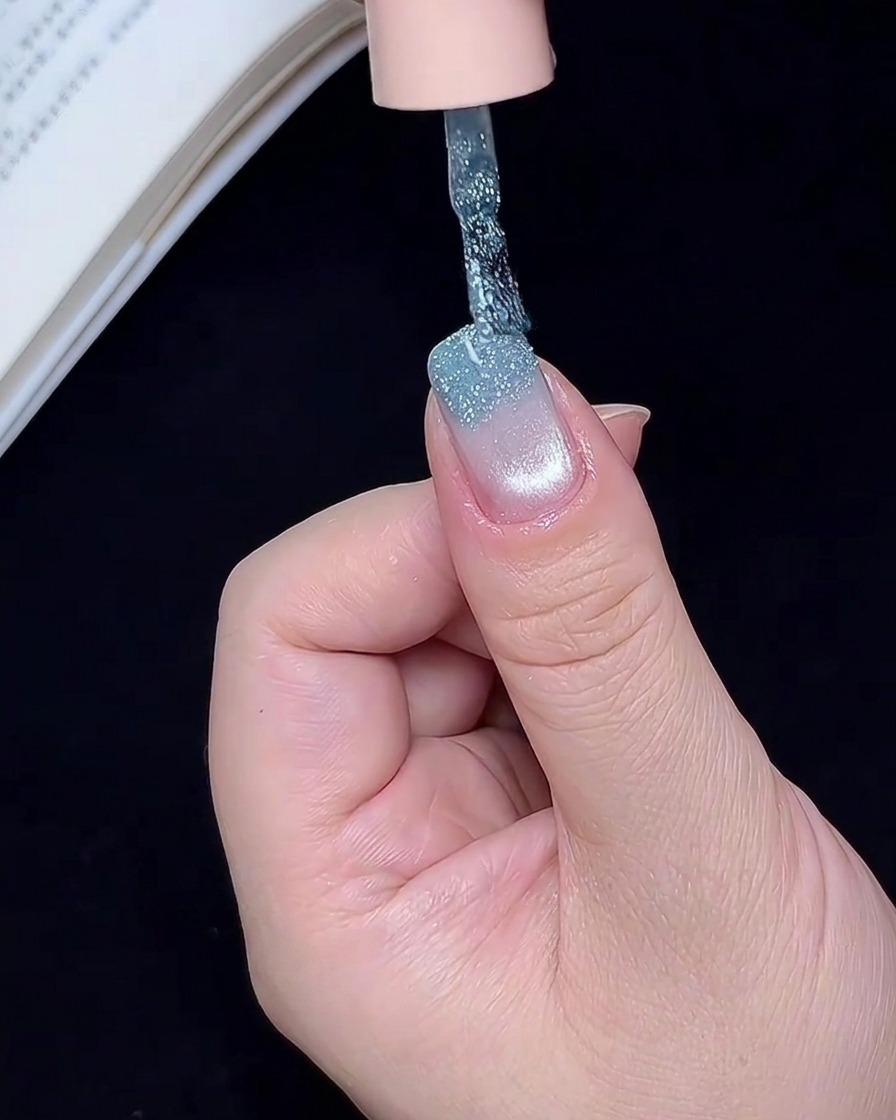 Un pennello per nail art che applica gel glitterato blu sul bordo libero dellunghia.