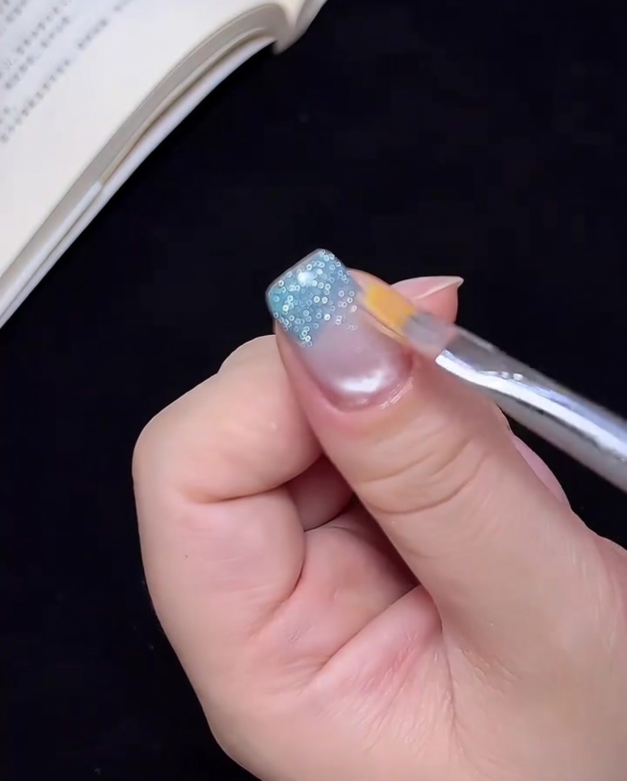 Un pennello pulito che trascina leggermente il gel glitterato blu verso lalto per creare un effetto ombré.