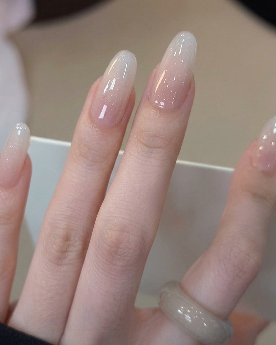Un pennello che applica un top coat trasparente e lucido sullunghia sfumata bianco latte completata.