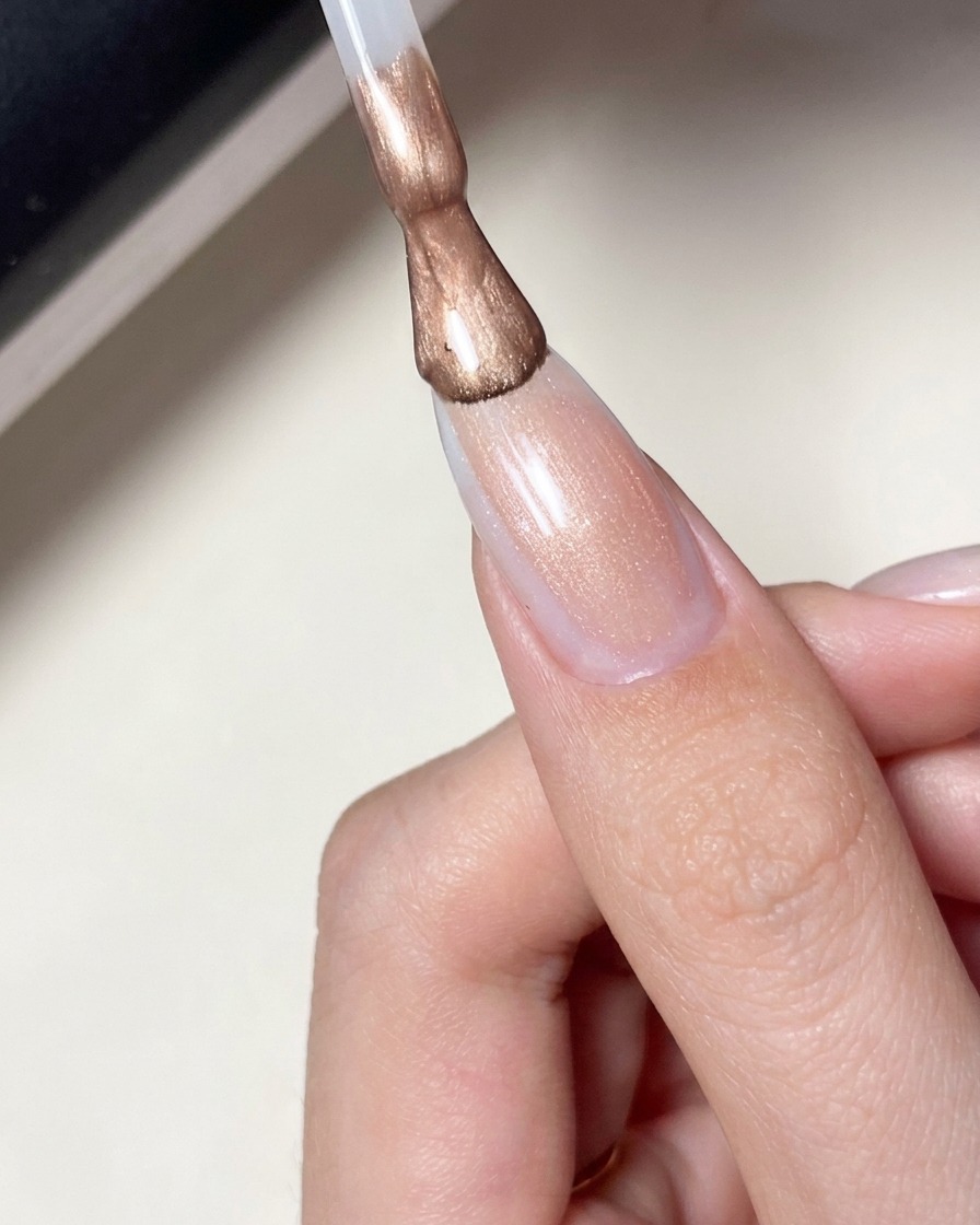Un pennello che applica uno smalto gel rosa latte e trasparente su ununghia con design a stella.