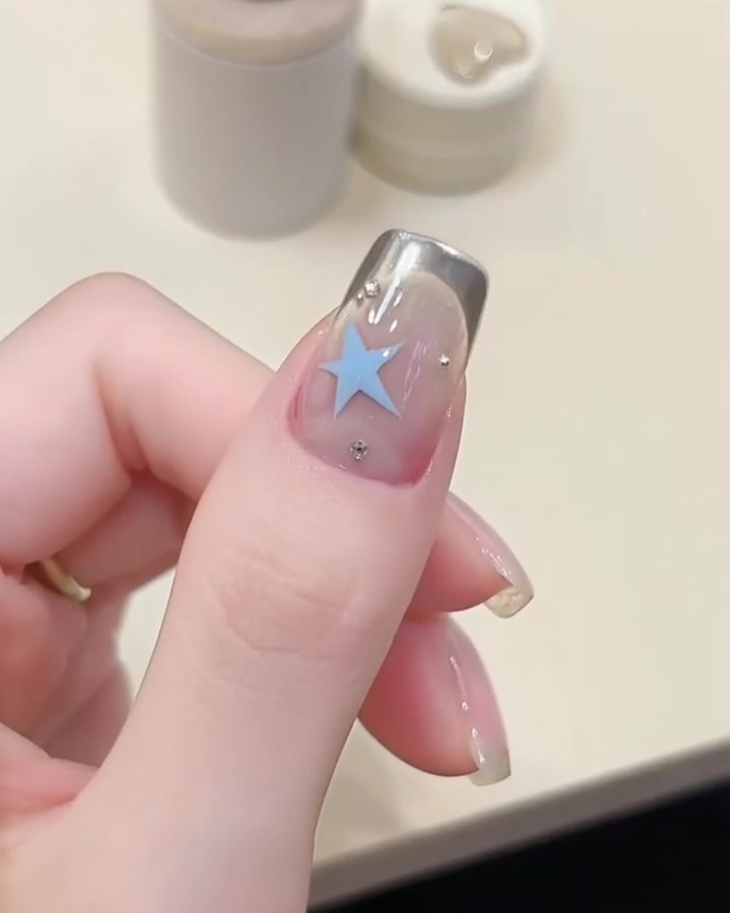 Un applicatore in spugna che applica polvere chrome argento sulla punta di ununghia sopra uno stencil.