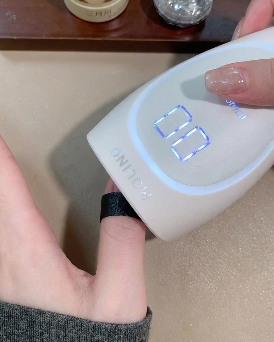 Una mano inserita sotto una lampada LED portatile per unghie per polimerizzare il gel.