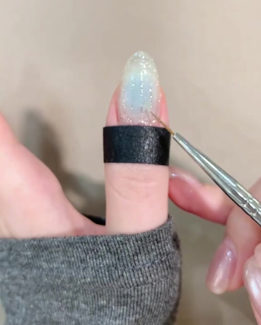 Una pinzetta posiziona una piccola stella dorata su ununghia decorata con glitter.