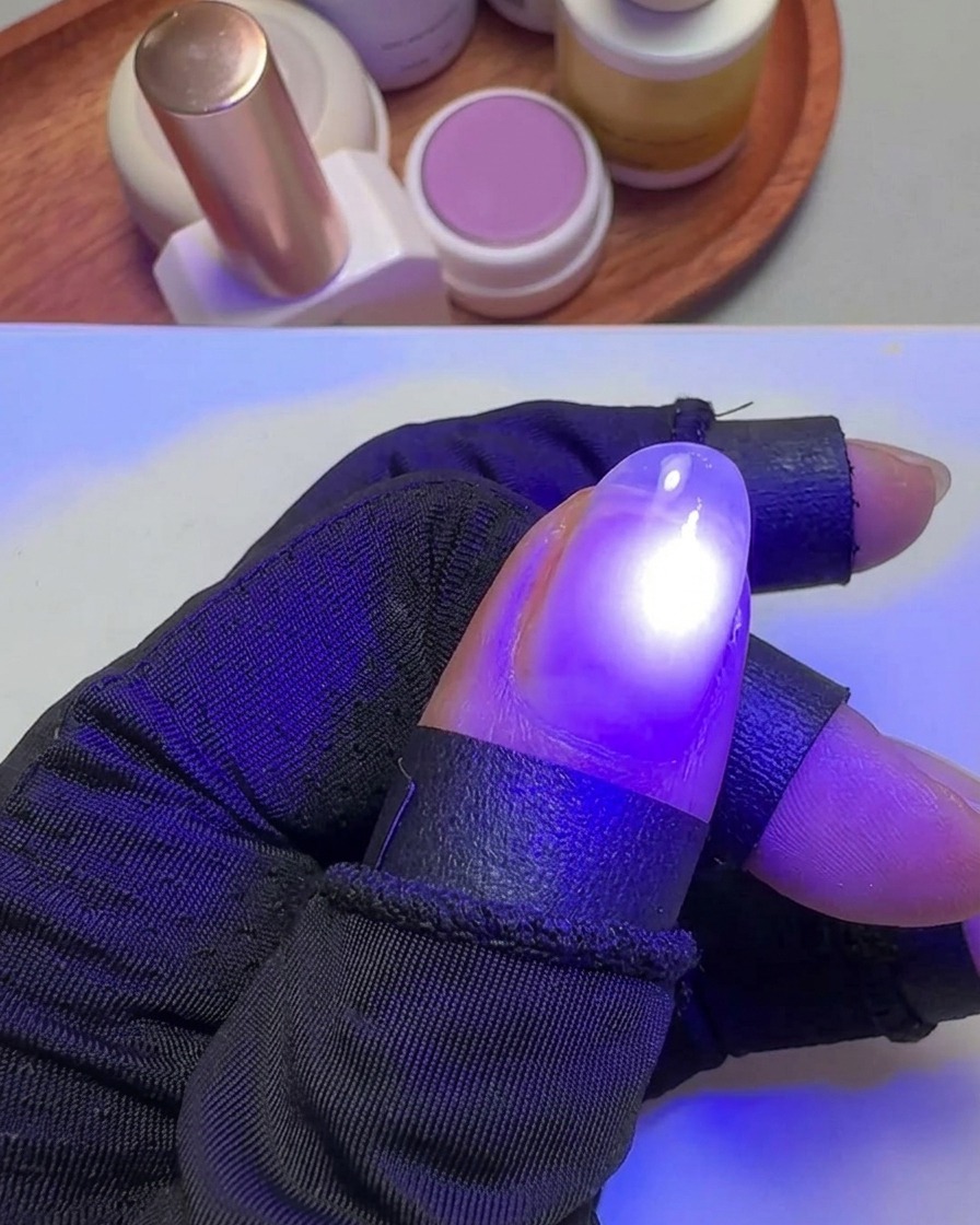 Una mano che tiene un pollice sotto una piccola luce UV viola mirata per polimerizzare lo smalto gel.